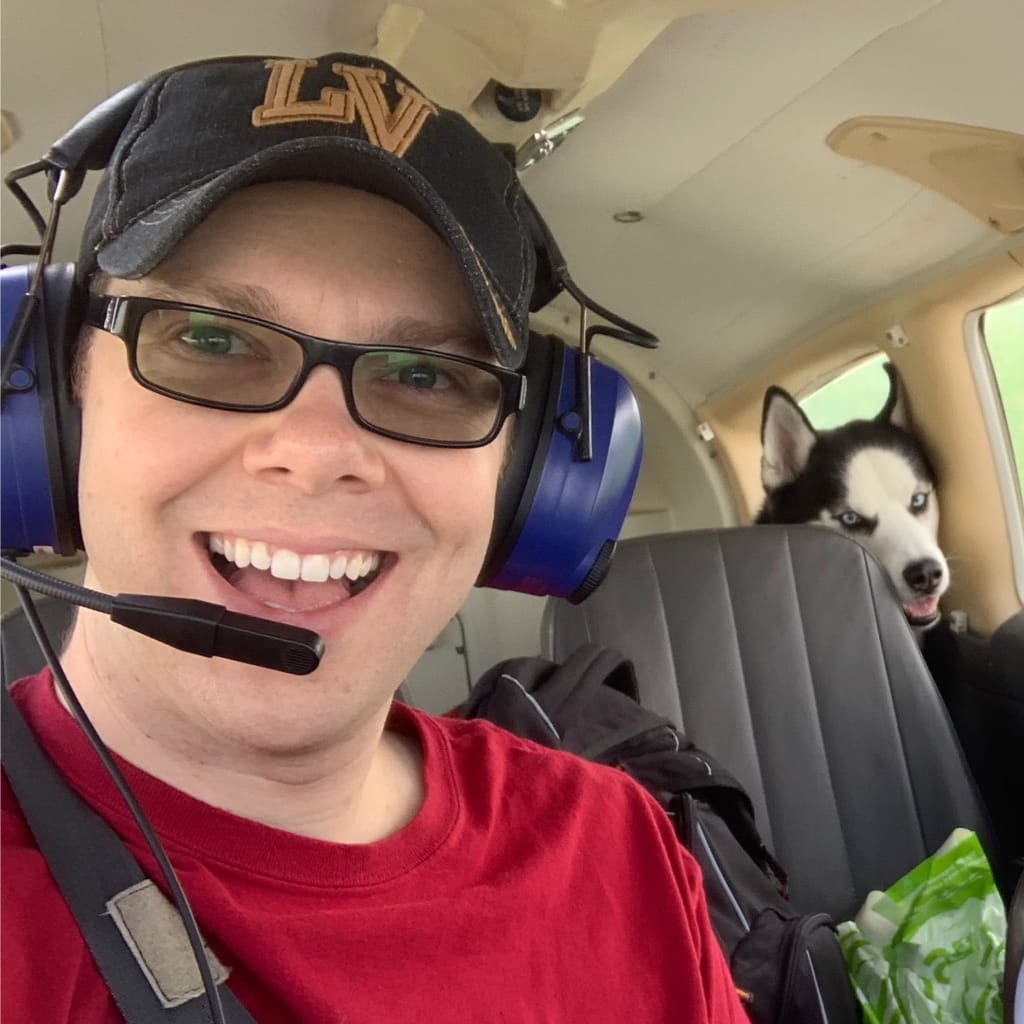 James Marshall in a private plane smiling at the camera with his husky, Bailey, in the back seat